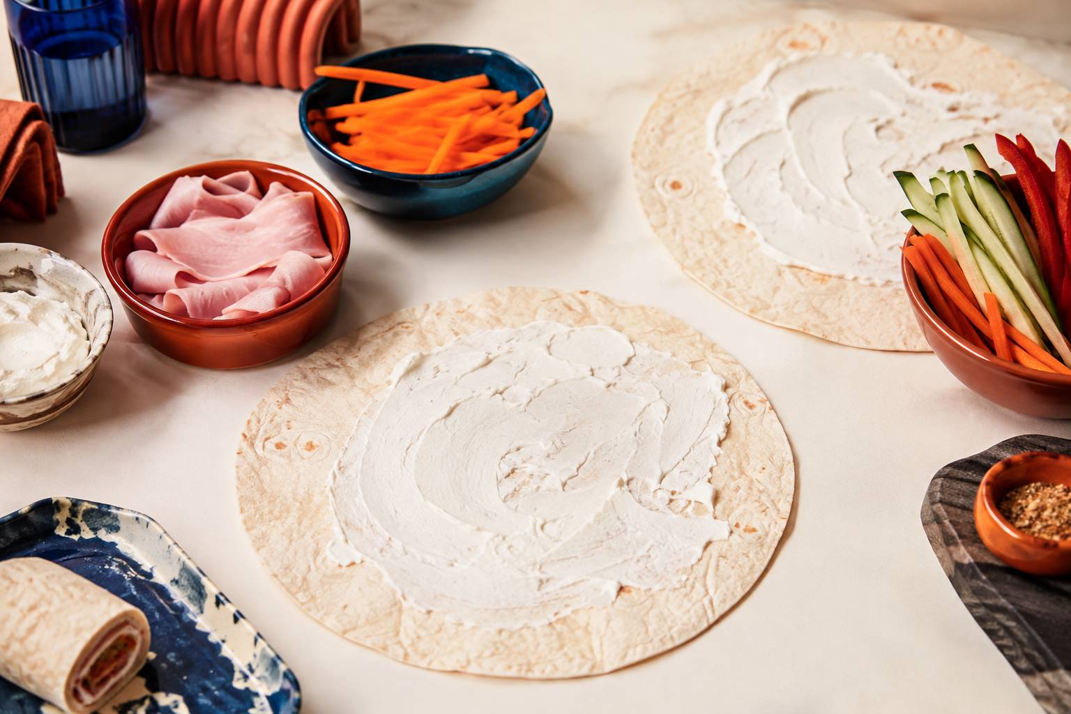 Tortillas tartinées de fromage frais avec garnitures de crudités en lanières dans des bols